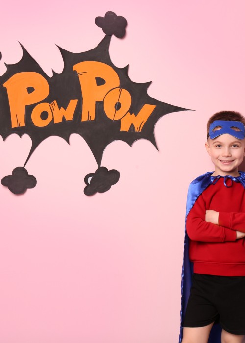 Cute boy in superhero costume on color background
