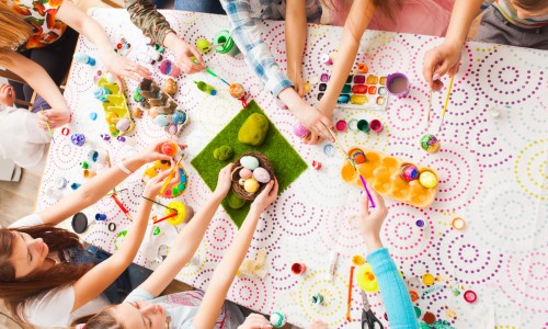Top view of kids hands holding Easter crafts and colored eggs. Group of children working together creating Easter decorations